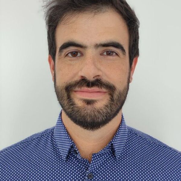 Portrait of Agustin Castiarena, a smiling man with dark hair and a beard, wearing a blue polka-dot shirt against a light background